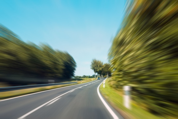 Blurred image of a rural road taken at high speed, illustrating the dangers of speeding and loss of control on curved or two-lane highways.