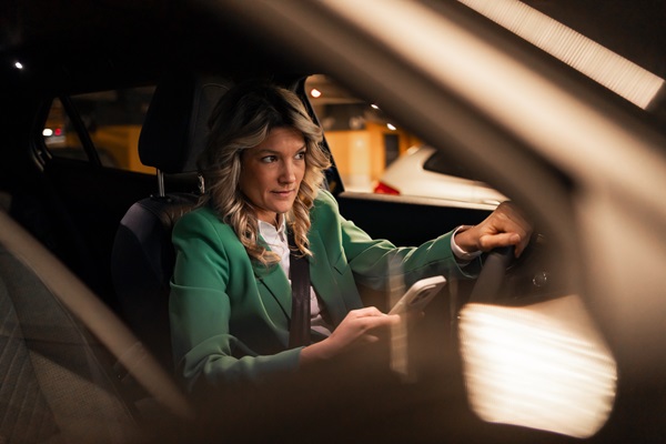 A driver in a green blazer looking down at a smartphone while behind the wheel at night, illustrating a violation of Maine's hands-free driving laws that often leads to serious crash claims.
